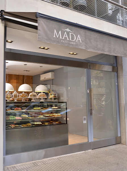 Frente del local de Mada Patisserie visto desde la vereda en el barrio de Belgrano, mostrando la vidriera con tortas y el cartel de la marca.